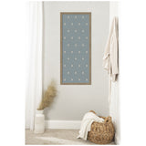 Tall blue rectangular pinboard with small white floral block prints evenly spaced, framed in natural wood and mounted on a light gray wall above beige carpet.