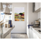 Abstract landscape canvas with soft pastel hills and earthy tones framed and hung on a white wall in a modern kitchen featuring gray stone countertops and ceramic tableware.