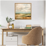 Framed Sylvie Rolling Hills painting depicting a soft green and gold abstract landscape with cloudy sky, hanging above a minimalist wooden desk with neutral decor.