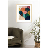 Framed minimalist abstract art on a white wall featuring overlapping jewel-toned semicircles in blue, green, orange, and pink above an olive-green armchair and potted plant.