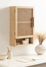 Light wood wall cabinet with woven rattan door and open cubby shelf below, mounted above a white desk with neutral decor.