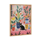 Framed whimsical painting of various colorful potted houseplants on a pink background with a black cat sitting among the plants, featuring bold leaves and geometric pot patterns.