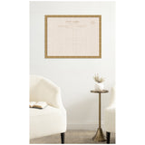 Vintage linen fabric pinboard framed in gold hanging on white wall between two cream armchairs and a brass pedestal table with white vase and dried flowers.