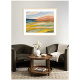 Abstract landscape painting with layered horizontal waves in blue, beige, orange, green, and yellow tones, framed and hung above a cozy seating area with two dark chairs and a round wooden table.