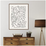 Abstract black continuous line art on white canvas framed in brown wood, hanging above vintage wooden dresser with woven basket and floor lamp with dark shade
