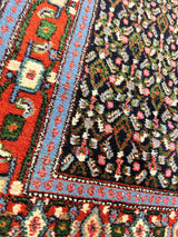 Close-up of a vintage Persian Senneh runner rug showing intricate floral patterns on a dark background with red, blue, and green geometric borders