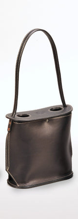 Dark brown leather tote with a single curved handle attached to a flat top featuring two circular cutouts, stitched with contrasting light thread.