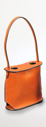 Smooth orange leather wine tote with two circular openings on top and a single stitched handle, standing upright against a white background.