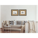 Two framed vintage postcard prints of London and Paris with brown mats hanging above a beige sofa adorned with patterned monochrome pillows and a chunky knit throw blanket.