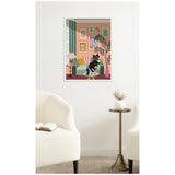 Framed canvas print of a black cat sitting on a green sofa surrounded by pink walls, potted palm, and various colorful abstract artworks in a cozy living room setting.