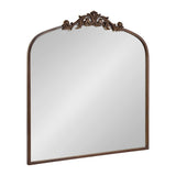 Rectangular mirror with a rounded arch top and ornate dark bronze scrollwork detail centered on the top edge, framed in matching bronze.