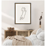 Minimalist black line drawing of a dachshund dog jumping, framed in black with a gold inner border, hanging above a bed in a light, neutral-toned room.