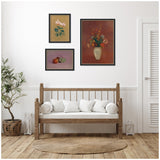Three framed art prints above a wooden bench with white cushions, including a floral bouquet in a vase and still life with fruit, set in a minimalist room with a plant and lanterns.