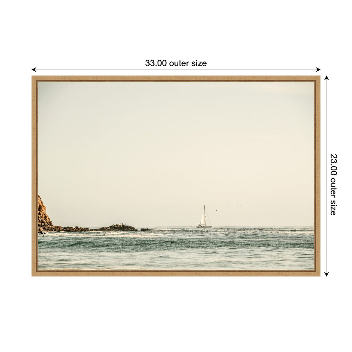 Sailboat on calm ocean near rocky coastline under a pale sky, framed in light wood with outer size dimensions 33 by 23 inches.