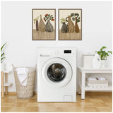 Two framed canvas prints above a white front-loading washer show stylized brown and beige vases with green and orange plants on a striped brown surface.