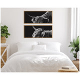 Two framed black-and-white canvas prints of Scottish Highland cattle heads, arranged vertically above a white bed in a minimalistic bedroom with green plants.