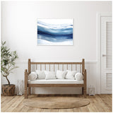 Framed abstract art print with flowing blue and white horizontal waves above a wooden bench with white cushions, set against a white wall in a minimalist room.
