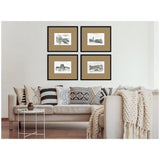 Four framed vintage black-and-white European architectural sketches with brown mats arranged in a 2x2 grid above a beige sofa with patterned pillows and a chunky knit throw.
