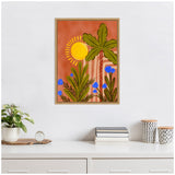 Framed canvas with stylized tall palm tree, yellow sun, green leaves, and blue flowers on an orange textured background, hanging above a white desk with plant and decor.
