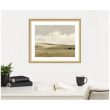 Soft beige and gray landscape painting depicting gentle rolling hills under a cloudy sky, framed in a light wood frame above a white desk with books, plant, and cup.