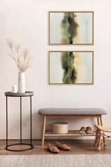 Two framed abstract paintings with soft green, beige, and black tones hang vertically over a wooden bench with gray cushion in a minimalist room.