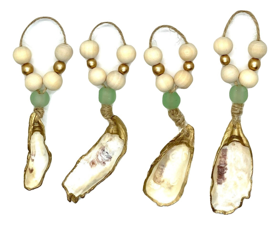 Four hanging oyster shell ornaments accented with natural wood and gold beads and a single green bead, each suspended on a looped twine string.