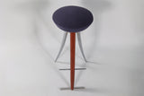 Modernist bar stool with a round dark blue cushioned seat, wooden central support, and three curved silver metal legs extending outward.