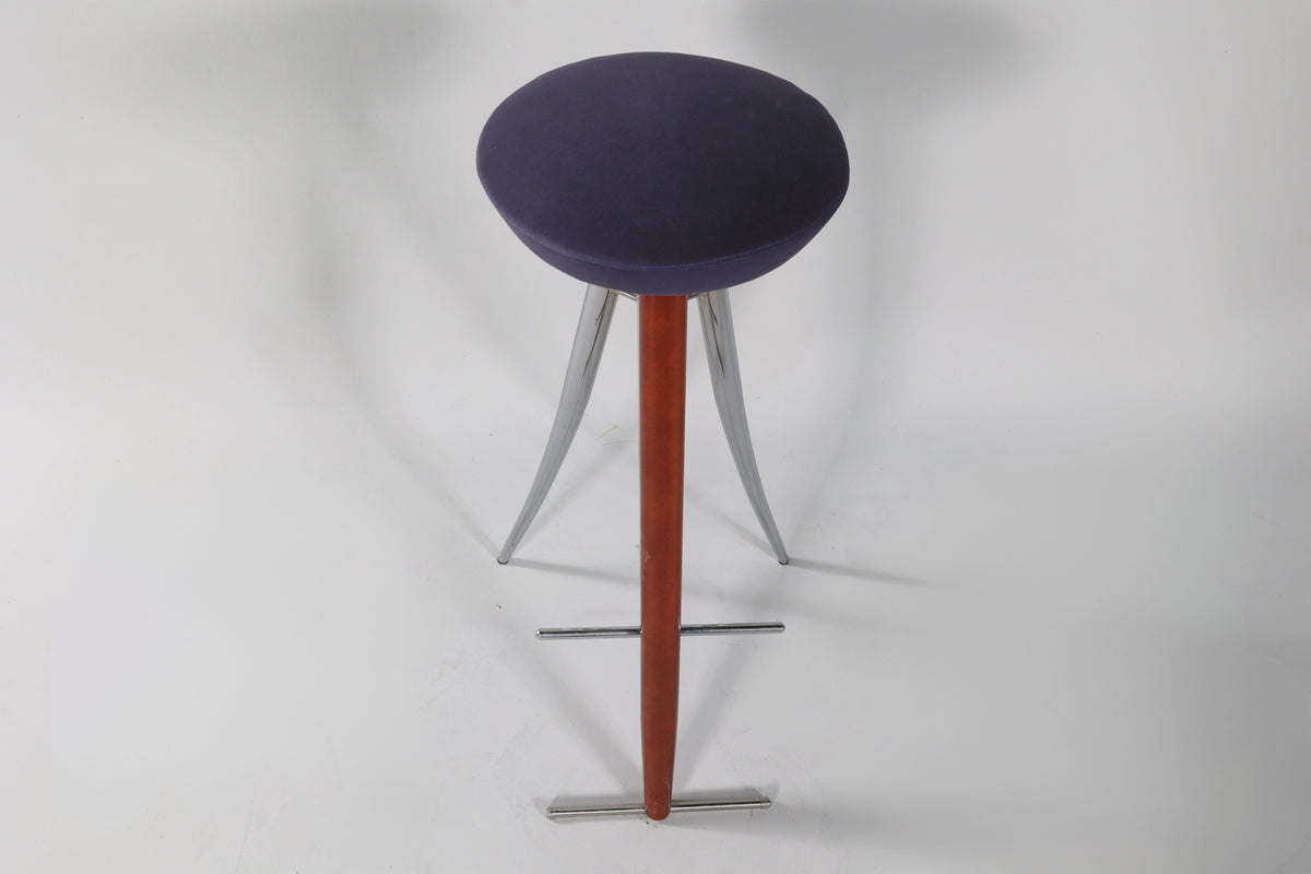 Modernist bar stool with a round dark blue cushioned seat, wooden central support, and three curved silver metal legs extending outward.