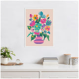 Framed canvas with a colorful abstract floral bouquet in a striped pink and purple vase on a beige background, hanging above a white desk with books, plant, and patterned containers.