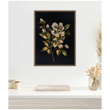 Framed canvas with cream and blush flowers and green leaves on a dark background, hanging above a white desk with neutral decorative items and dried plants.