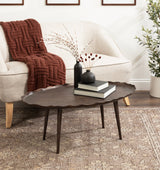Dark wood oval coffee table with a gently scalloped edge and tapered legs, topped with two black vases and stacked books, in front of a cream sofa with a knitted rust throw.