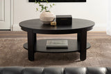 Round dark wood coffee table with a lower shelf, decorated with a textured beige vase holding green branches and a small dark box, set on a woven area rug.