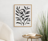 Black leafy botanical silhouette print in simple wood frame hanging on white wall above gold side table with white bowl and a tall green grass plant beside it