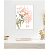 Framed canvas print of delicate pink hydrangea flowers with green leaves on a white wall, above a white desk with beige and cream decor accents.