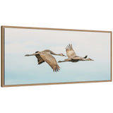 Framed canvas wall art depicting two cranes flying against a pale sky, set in a beaded rustic natural wood frame.