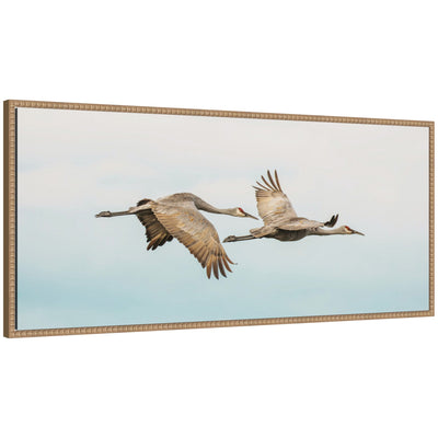 Framed canvas wall art depicting two cranes flying against a pale sky, set in a beaded rustic natural wood frame.