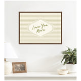 Framed sage green and beige horizontal striped canvas wall art with retro-style diamond shape center and "Love You More" script text, mounted above a white table.