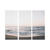 Three-panel canvas wall art depicting a serene ocean shore with gentle waves under a pale pink and blue sky at sunrise or sunset.