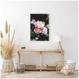 Light pink roses with dark green leaves on a black background, framed and hung above a rustic wooden console table in a neutral-toned room.