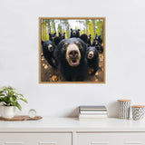 Framed photo of eight black bears in a forest, one smiling in the front with a close-up perspective and others behind among tall trees and fallen leaves.