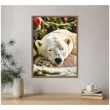 Framed canvas photo of a white polar bear sleeping peacefully beneath a decorated Christmas tree with red ornaments, displayed on a pale wall above a wooden table.