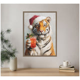 Framed canvas painting of a tiger wearing a red Santa hat holding a festive cocktail glass garnished with holly, displayed on a light wall above a wooden table.