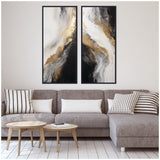 Two vertical framed abstract canvases featuring swirling black, white, and gold textures above a gray sectional sofa with striped and solid pillows, beside light wood nesting tables.