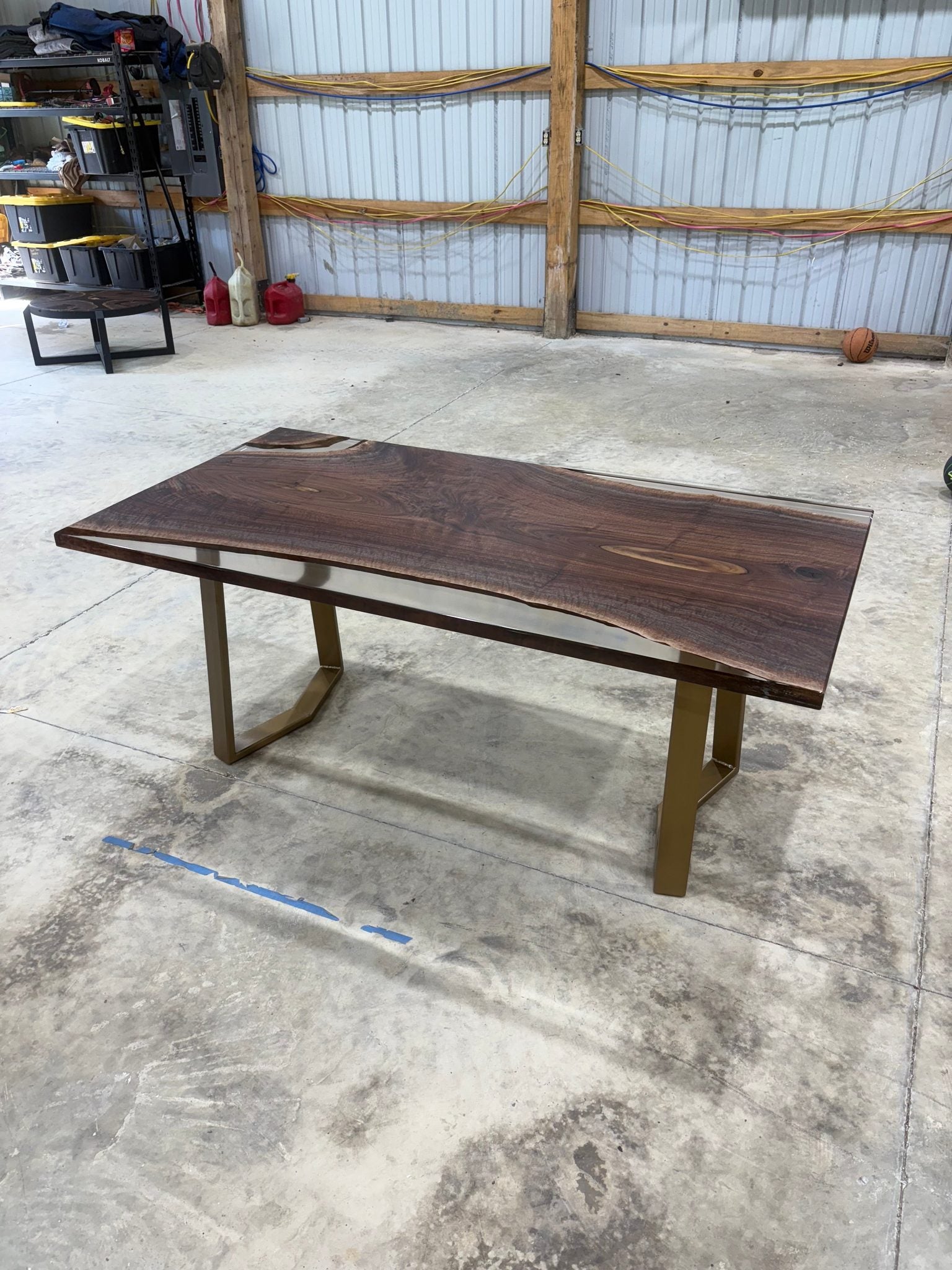 Handcrafted walnut slab table with clear resin finish and gold legs in a workshop setting