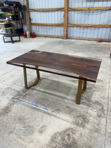 Handcrafted walnut slab table with clear resin finish and gold legs in a workshop setting