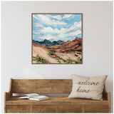 Square framed canvas depicting a desert landscape with mountains and a cloudy sky in soft blues, pinks, and earthy browns above a wooden bench with a beige cushion reading 'welcome home'