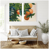Two-panel framed canvas art showing vibrant oranges hanging on leafy green branches against a light background above a wooden bench with black and white checkered cushions.