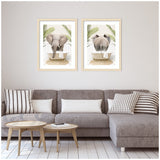 Two framed prints side by side showing a grey elephant in a white bathtub with palm leaves, viewed from front and rear angles, above a gray sectional sofa.