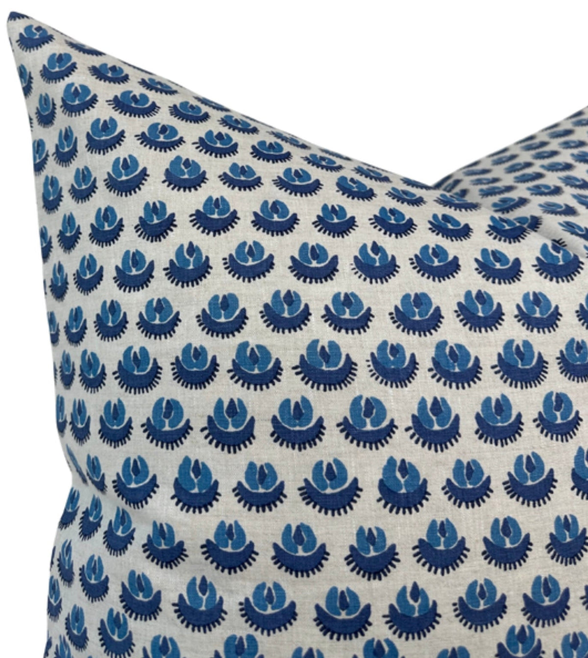 Close-up of a cream pillow cover patterned with repeating clusters of blue fan-shaped and circular motifs, showing fabric texture and sharp corner detail.