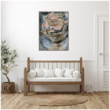 Abstract framed canvas with muted tones of blue, beige, and peach hangs above wooden bench framed by white cushions in minimalist room with plant and round woven rug.